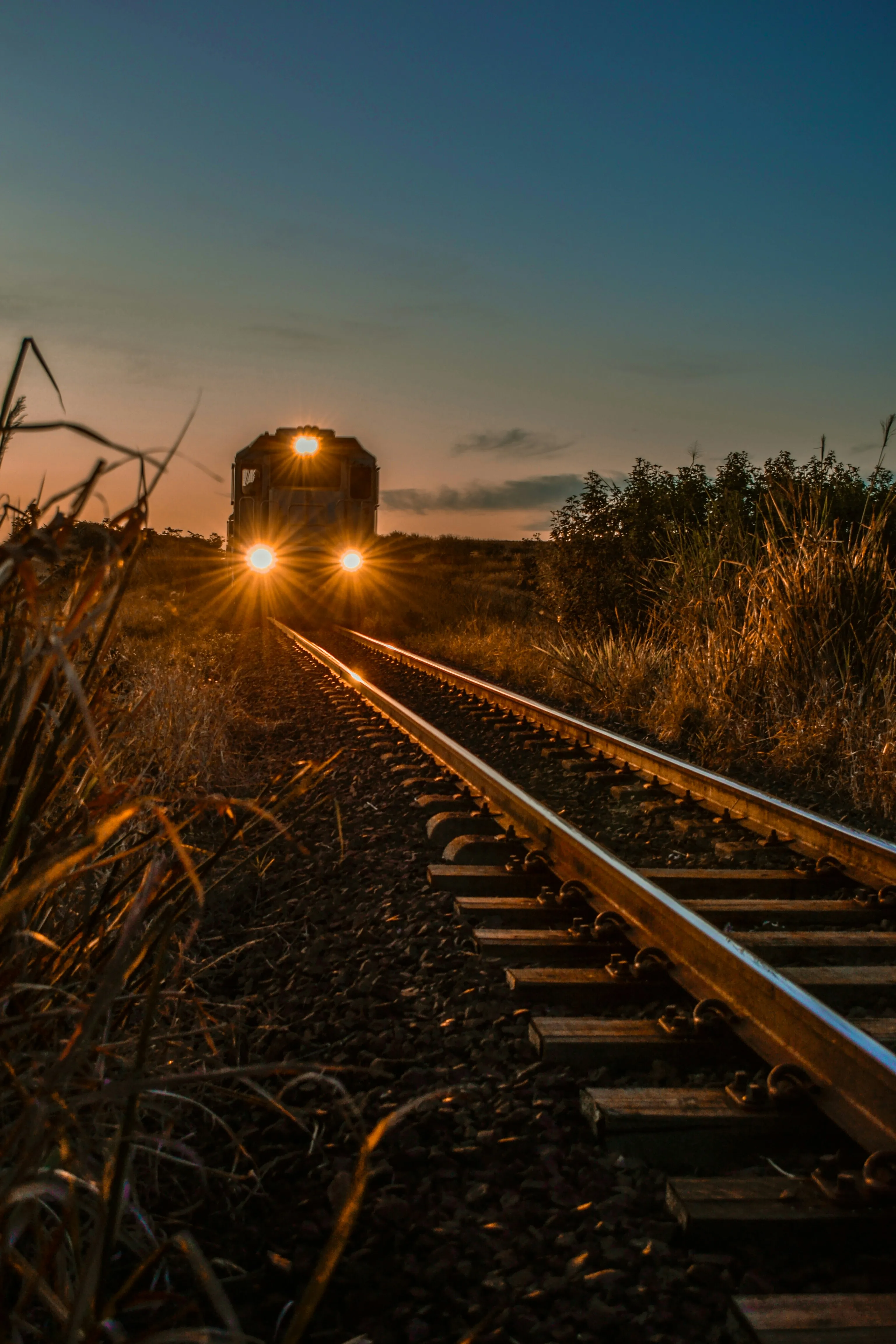 A locomotive's headlights approaching down the track at dusk